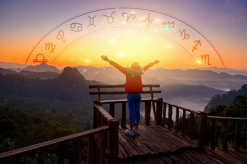 Woman with arms wide open looking at sunrise with zodiac signs in the sky