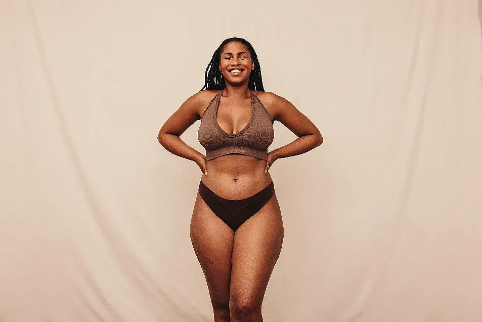 Self-love and happiness. Cheerful young woman smiling with her eyes closed while standing against a studio background. Body positive young woman embra