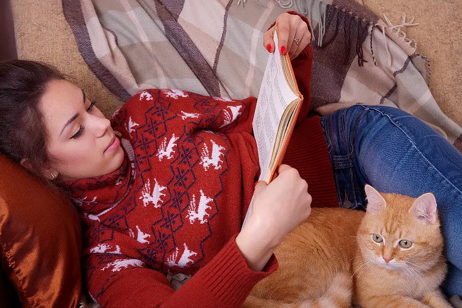 A woman snuggled on the sofa with her cat, reading a book