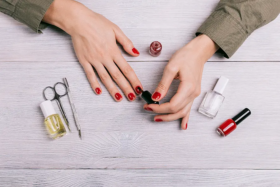 Top view of a woman doing a manicure and paint nails with red lacquer