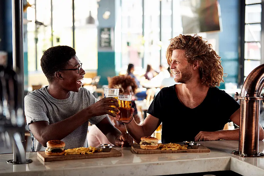 Two Male Friends Eating Food And Drinking Beer In Sports Bar