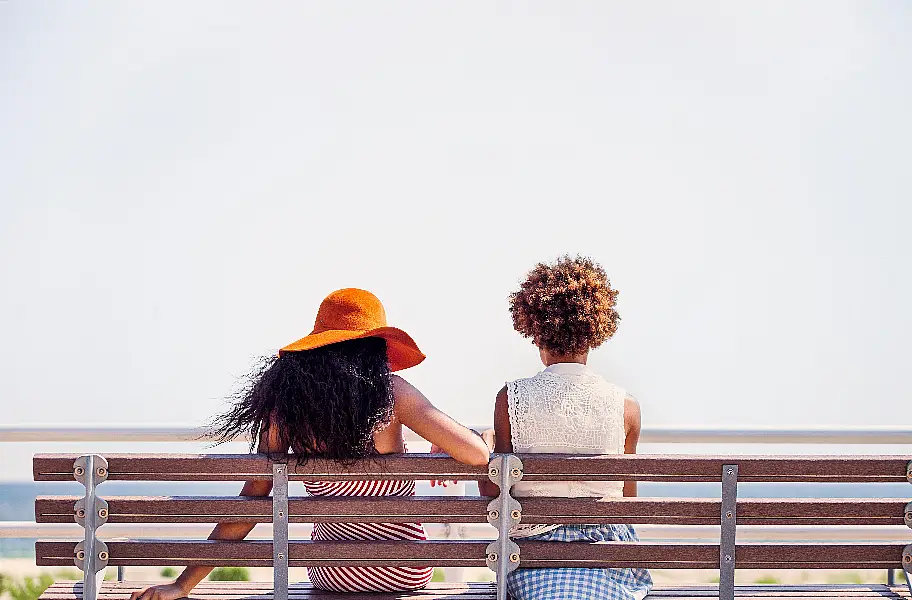 Female friends sitting on bench by sea