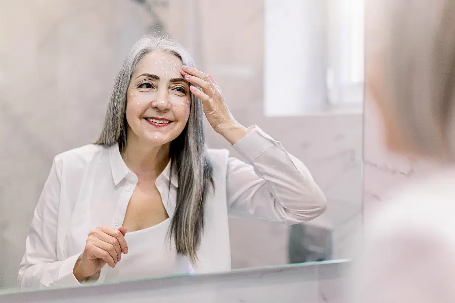 Woman applying skincare in bathroom mirror