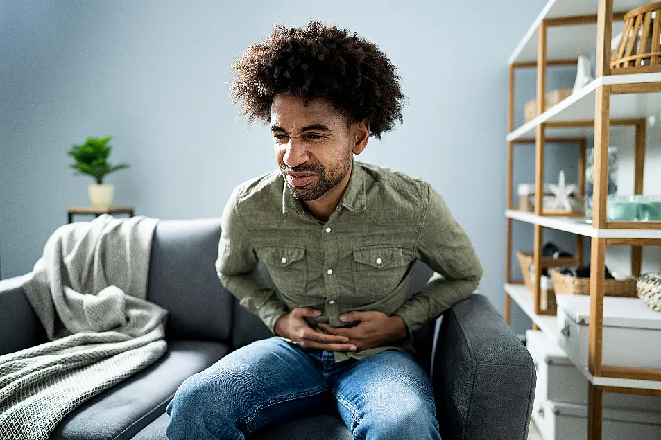 Black man sitting on a sofa clutching his stomach in pain