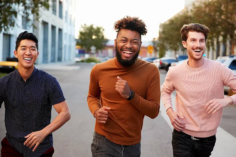 Male friends running down a street laughing together