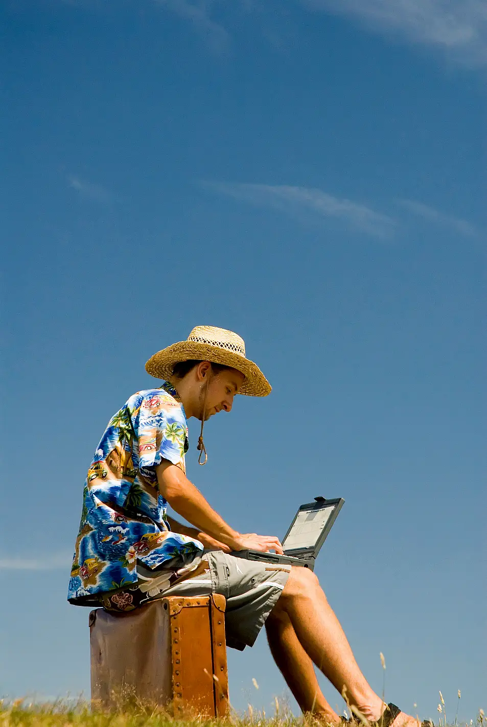 man sitting on old leather suitcase working on laptop