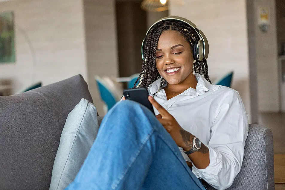 Woman listening to music on headphones at home lying on the sofa, looking happy and content