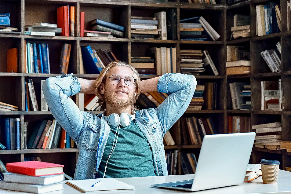 Man sitting at a desk in front of a bookcase, thinking and looking into the distance