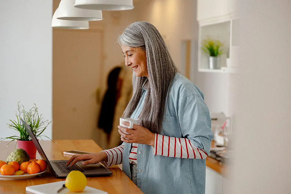 Woman drinking coffee in kitchen while using keyboard