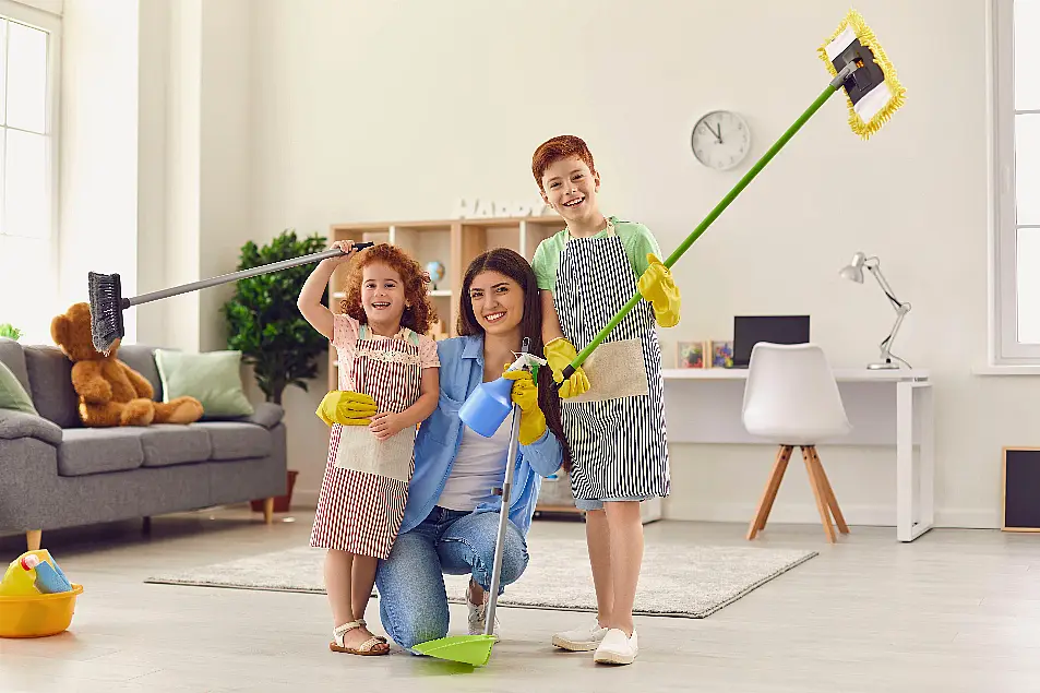 Happy mum and kids with floor mops and dustpan smiling and looking at camera after a big clear-out