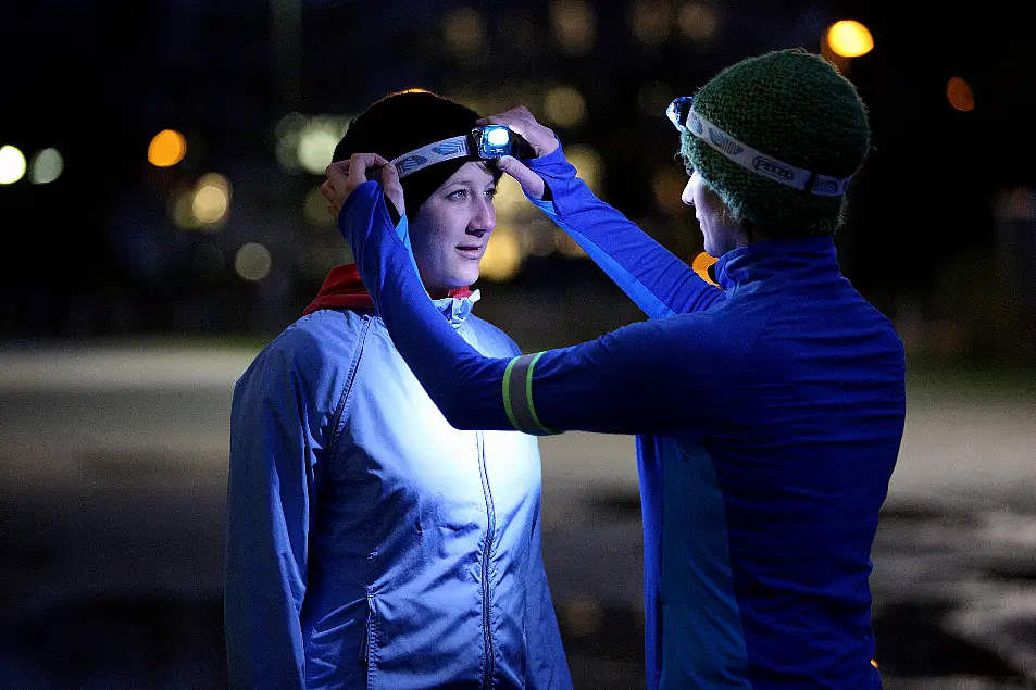 Two women taking a break from running in the dark to adjust their head torches