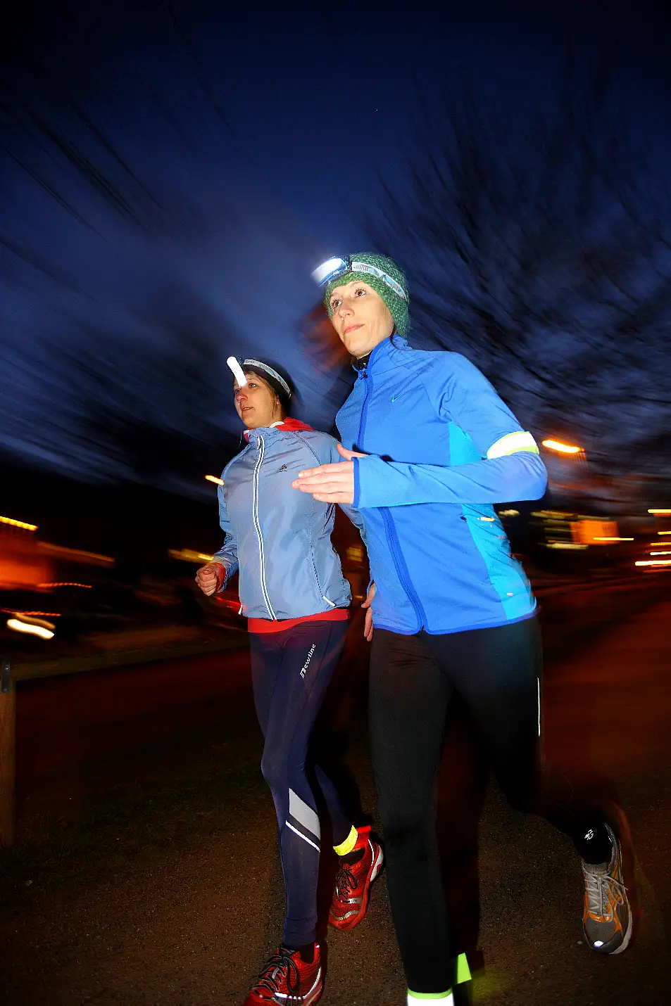 Two young women wearing reflective clothing jogging together at night 