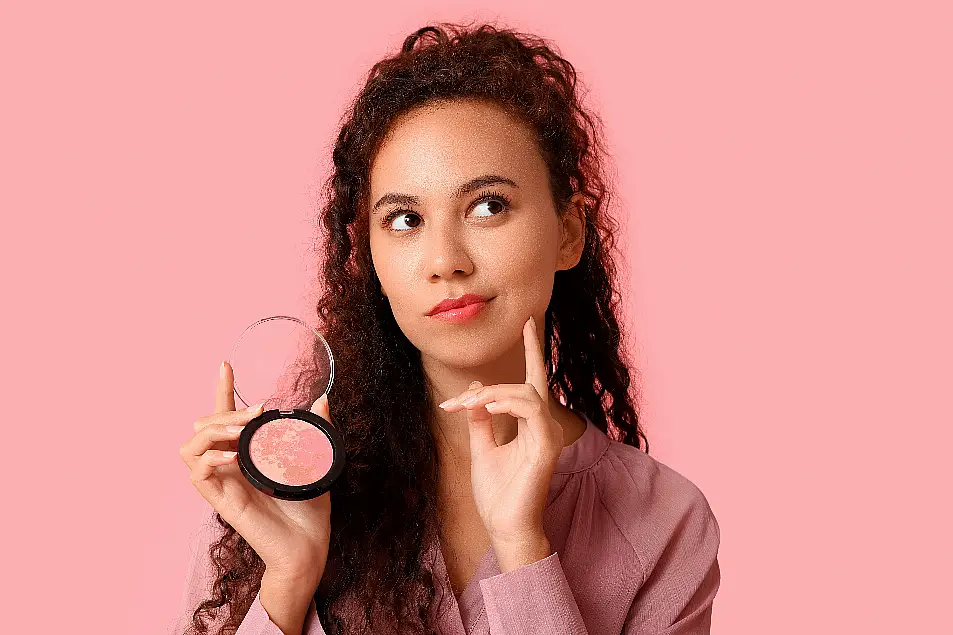 Woman poses with blush palette looking thoughtfully to the side