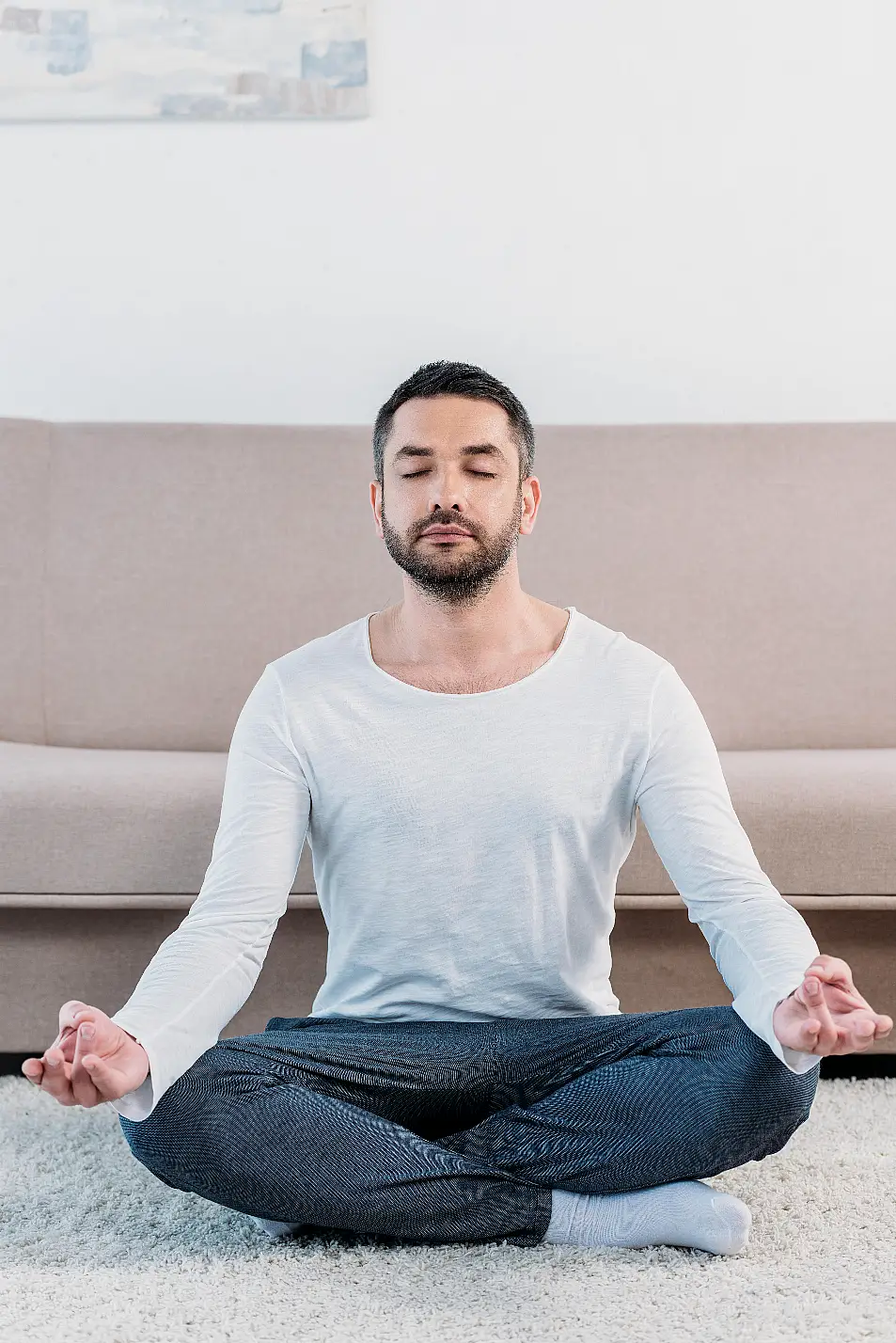 Man sat on the floor in a living room cross-legged meditating 