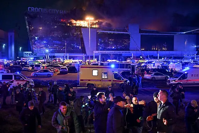 A man speaks to journalists as a massive blaze is seen over Crocus City Hall on the western edge of Moscow, Russia 