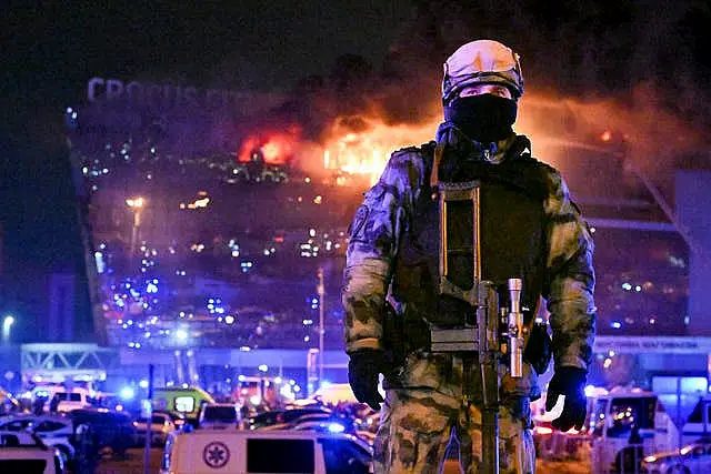 A Russian Rosguardia (National Guard) servicemen secures an area as a massive blaze seen over the Crocus City Hall on the western edge of Moscow, Russia