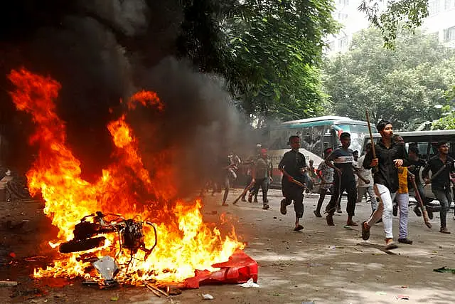 Men run past a burning vehicle inside the Bangabandhu Sheikh Mujib Medical University Hospital