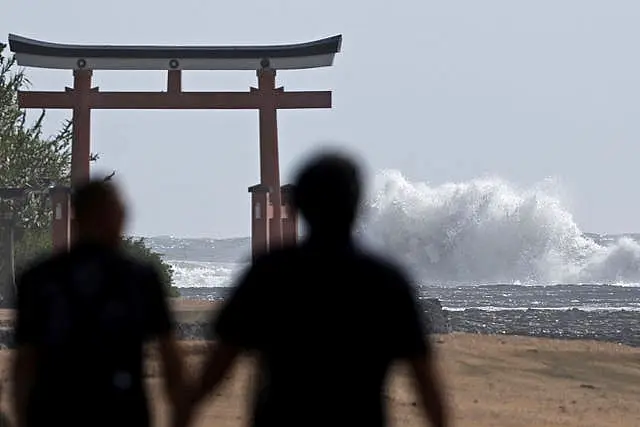 People walk near a 'torii' gate of a shrine while waves hit a coastal area in Miyazak