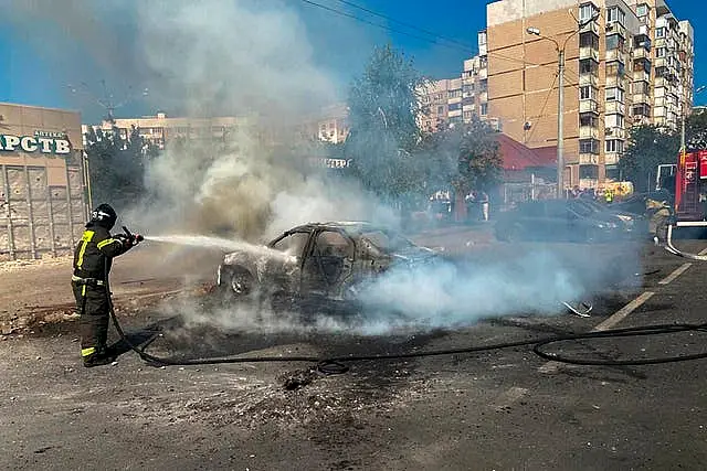 Firefighter sprays water hose at burning car on street