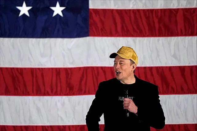 Elon Musk speaks in front of a giant Stars and Stripes flag