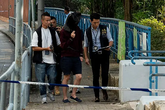 An unidentified person wearing a hood is escorted by police officers to the park where the body was found