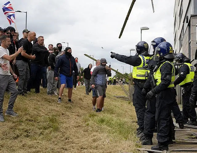 Ricky Hardman (left, bald head, black top and grey cargo trousers) standing with a group of men as objects are thrown towards police at the Holiday Inn Express in Rotherham, South Yorkshire 