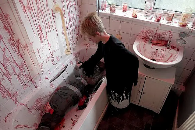 Nine-year-old Freddy holding a fake knife in a pretend blood-splattered bathroom